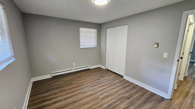 unfurnished bedroom with baseboard heating, a closet, baseboards, and dark wood-style floors