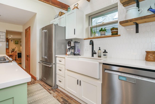 kitchen with a sink, open shelves, light countertops, brick floor, and appliances with stainless steel finishes