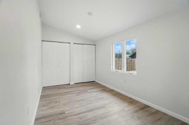 unfurnished bedroom featuring baseboards, light wood-style floors, vaulted ceiling, and two closets