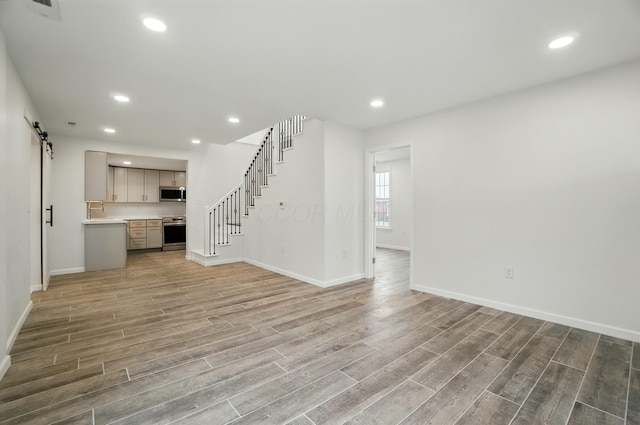 unfurnished living room featuring baseboards, a barn door, light wood-style floors, and stairs