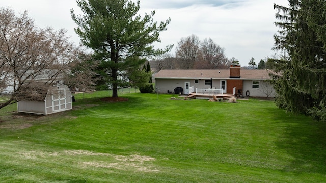 back of house featuring a chimney, a wooden deck, an outbuilding, a lawn, and a storage unit