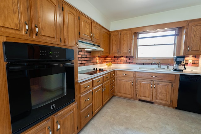 kitchen with tasteful backsplash, a sink, under cabinet range hood, brown cabinets, and black appliances