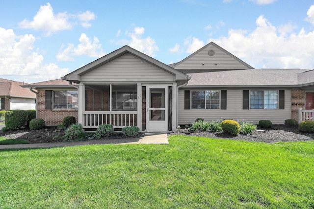 ranch-style house with a front lawn, a sunroom, brick siding, and roof with shingles