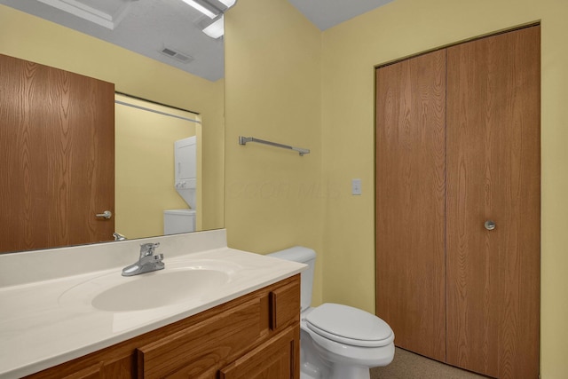 half bath with visible vents, stacked washer and clothes dryer, vanity, and toilet
