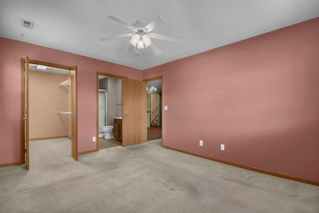 unfurnished bedroom with a walk in closet, visible vents, baseboards, and light carpet