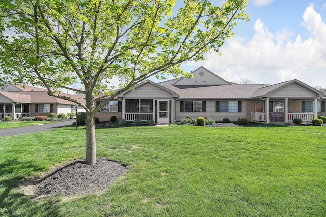 view of front of home with brick siding, a sunroom, a front lawn, and roof with shingles