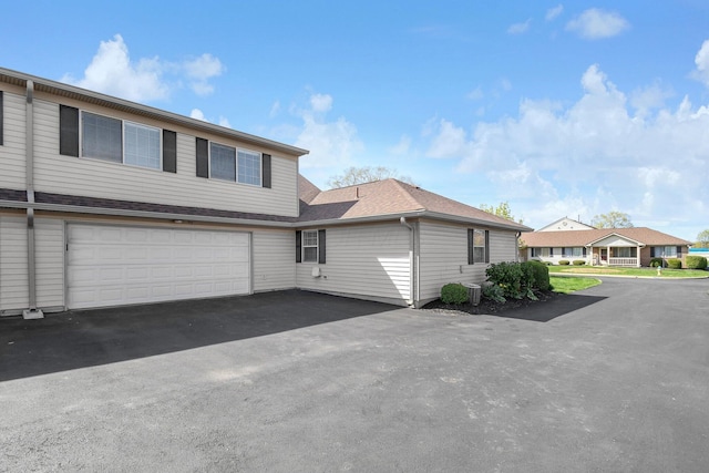 view of front of property with an attached garage, driveway, roof with shingles, and cooling unit