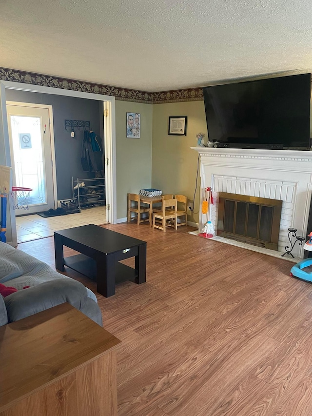 living room featuring a brick fireplace, wood finished floors, and a textured ceiling