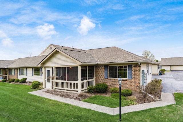 rear view of house featuring roof with shingles, a sunroom, a garage, brick siding, and a yard