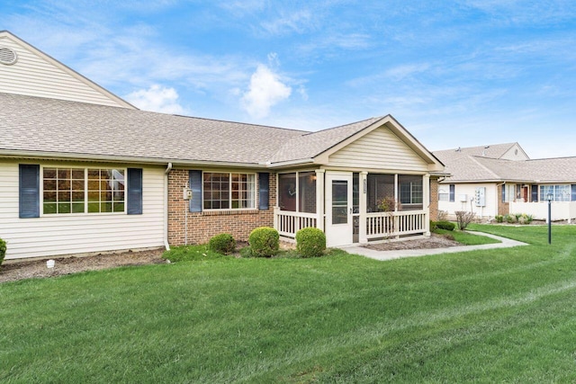 rear view of property with brick siding, roof with shingles, a yard, and a sunroom