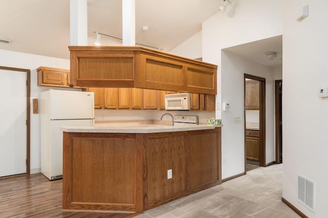 kitchen with visible vents, brown cabinetry, lofted ceiling, white appliances, and light countertops