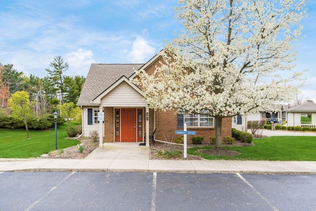 view of front of property featuring brick siding, a shingled roof, a front lawn, and uncovered parking