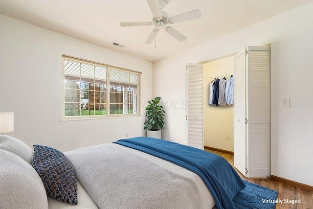 bedroom with a walk in closet, a ceiling fan, visible vents, wood finished floors, and baseboards