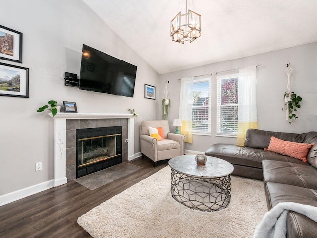 living area with baseboards, a chandelier, a tiled fireplace, dark wood-type flooring, and lofted ceiling