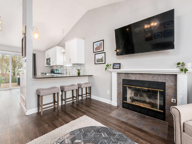 living area featuring visible vents, baseboards, a tiled fireplace, vaulted ceiling, and dark wood-type flooring