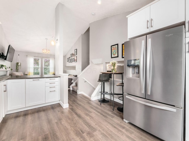 kitchen with white cabinetry, wood finished floors, stainless steel fridge, and vaulted ceiling