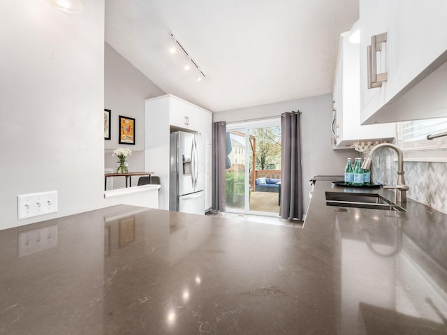 kitchen featuring track lighting, white cabinets, stainless steel refrigerator with ice dispenser, lofted ceiling, and a sink
