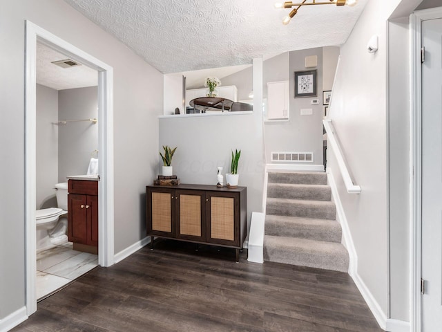 stairway with a textured ceiling, wood finished floors, and visible vents