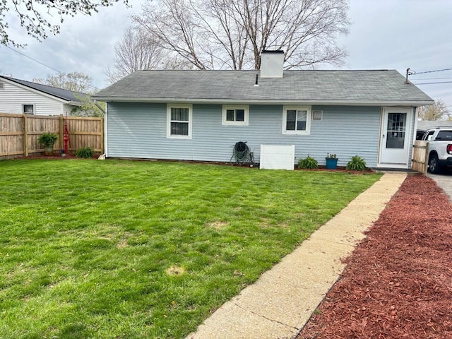 back of property with a lawn, a shingled roof, a chimney, and fence