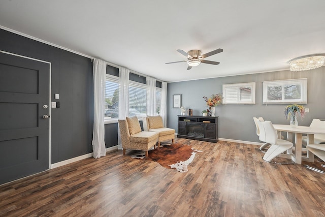 living area featuring wood finished floors, a ceiling fan, baseboards, and ornamental molding
