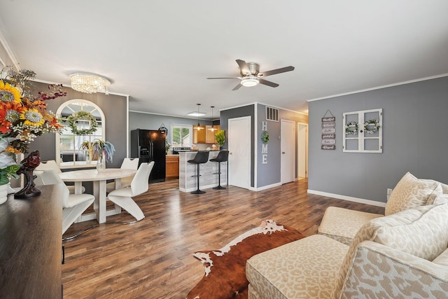living area with dark wood finished floors, visible vents, ornamental molding, and ceiling fan with notable chandelier