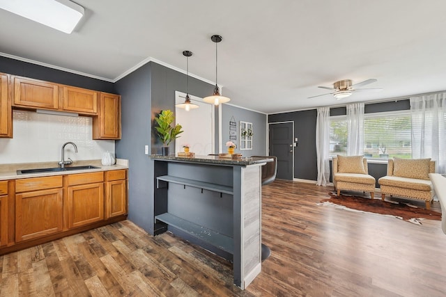 kitchen featuring a sink, brown cabinetry, backsplash, ornamental molding, and dark wood-style floors