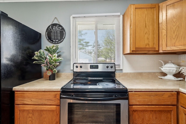 kitchen with light countertops, freestanding refrigerator, stainless steel range with electric stovetop, and decorative backsplash