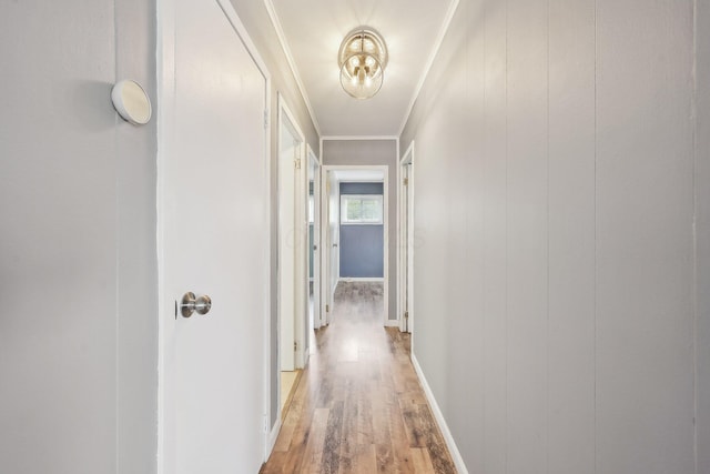 hallway with light wood-type flooring, crown molding, and baseboards