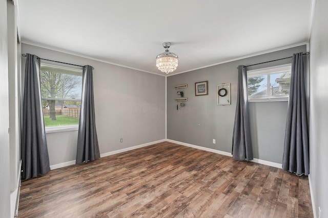 empty room with a notable chandelier, baseboards, ornamental molding, and wood finished floors