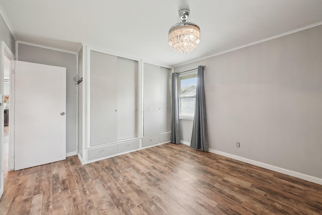 unfurnished bedroom with crown molding, wood finished floors, a chandelier, two closets, and baseboards