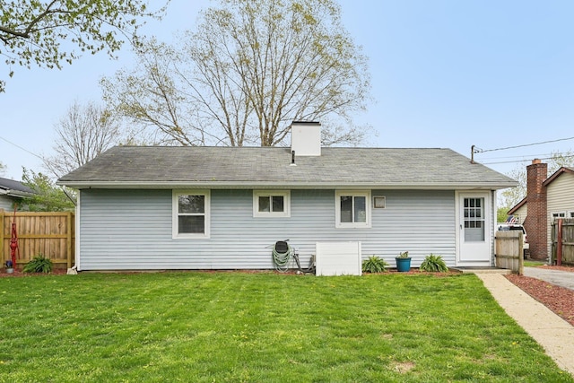 back of property featuring a lawn, roof with shingles, fence, and a chimney