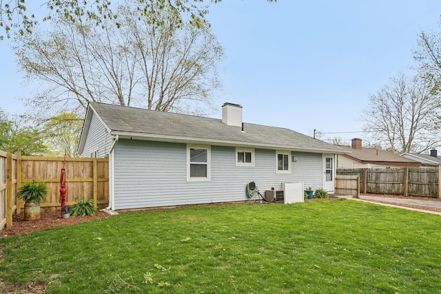 back of house with a lawn, a chimney, and a fenced backyard