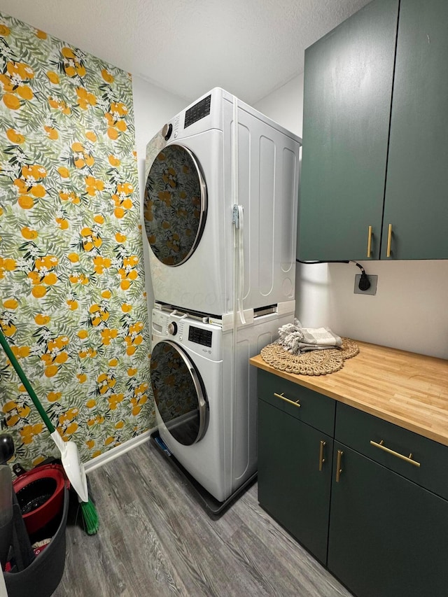laundry room featuring baseboards, stacked washer and clothes dryer, wood finished floors, wallpapered walls, and cabinet space