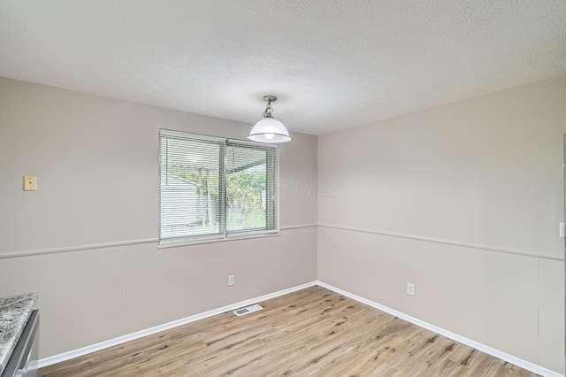 unfurnished dining area featuring light wood-style floors, baseboards, and a textured ceiling