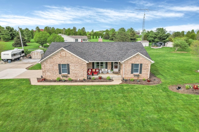ranch-style house with covered porch, a front yard, roof with shingles, brick siding, and a storage shed