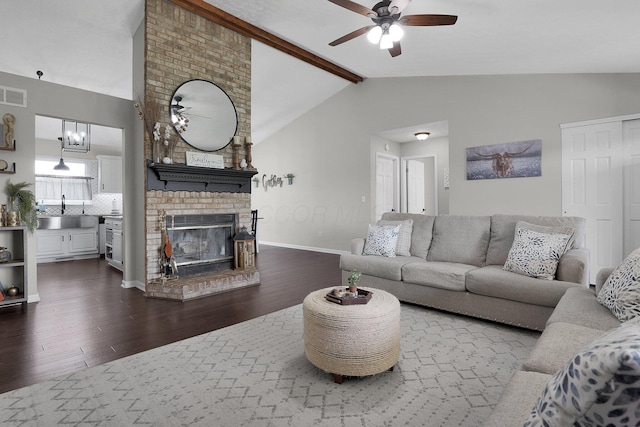 living area featuring dark wood-type flooring, lofted ceiling with beams, a brick fireplace, and ceiling fan