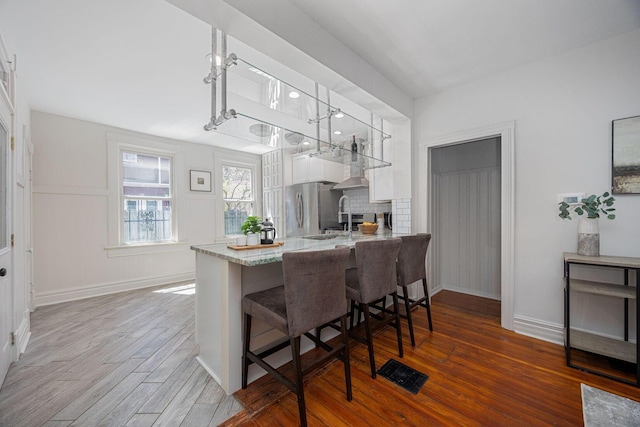 kitchen featuring a kitchen breakfast bar, wood finished floors, freestanding refrigerator, a peninsula, and white cabinetry