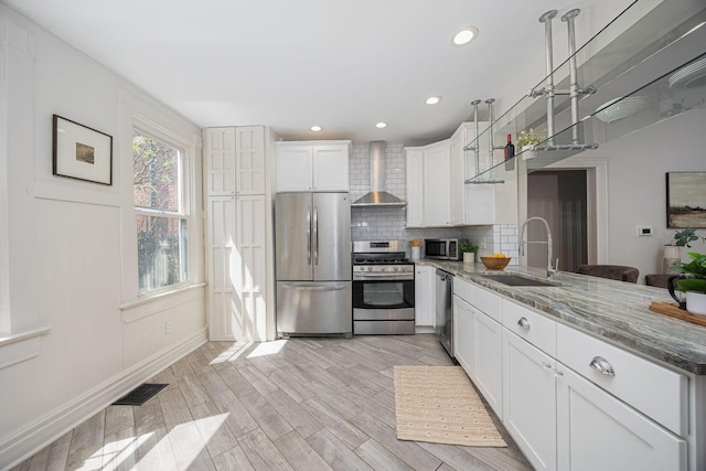 kitchen featuring wall chimney range hood, light stone counters, a sink, stainless steel appliances, and visible vents
