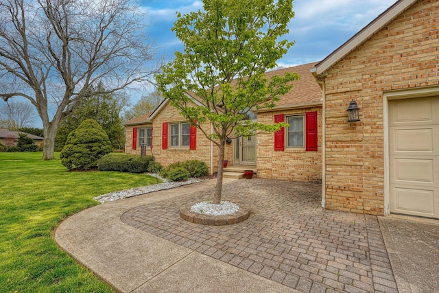 exterior space featuring brick siding, a front yard, roof with shingles, and entry steps