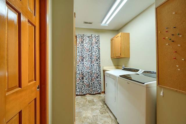 clothes washing area featuring independent washer and dryer, stone finish flooring, visible vents, baseboards, and cabinet space