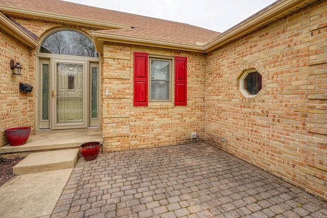 property entrance featuring a shingled roof and brick siding