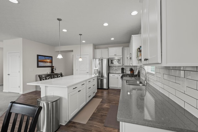 kitchen with white cabinets, appliances with stainless steel finishes, a sink, backsplash, and a kitchen island