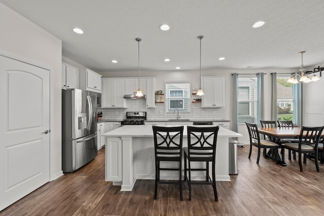 kitchen with a center island, under cabinet range hood, white cabinets, backsplash, and stainless steel appliances