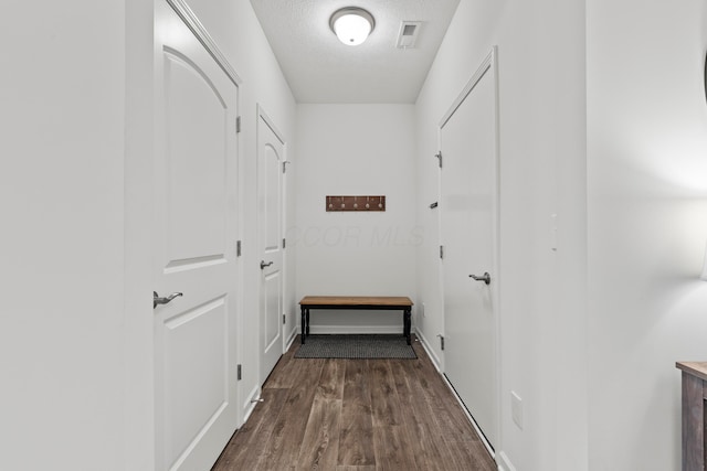 hallway featuring dark wood-type flooring, a textured ceiling, baseboards, and visible vents