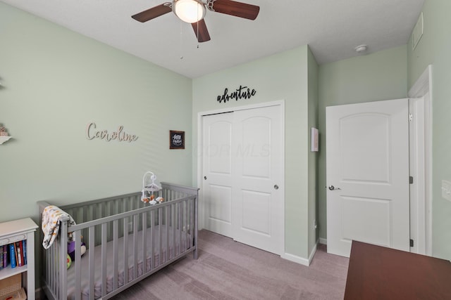 carpeted bedroom with baseboards, a crib, ceiling fan, and a closet