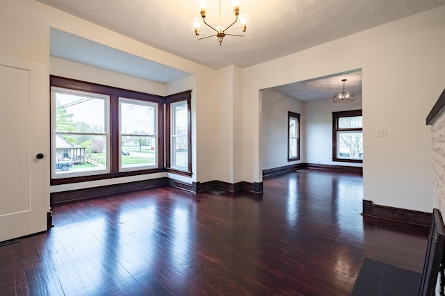 unfurnished living room featuring baseboards, an inviting chandelier, and wood finished floors