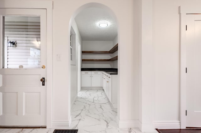 corridor with arched walkways, marble finish floor, baseboards, and a textured ceiling