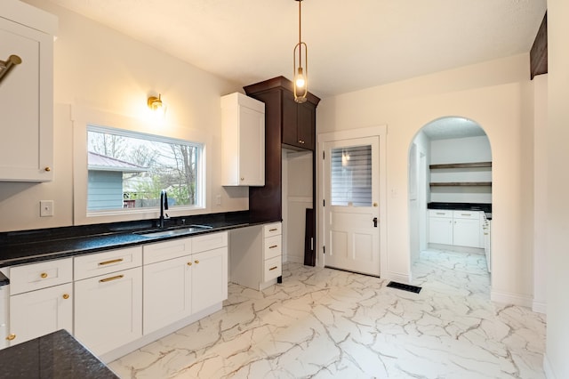 kitchen featuring pendant lighting, arched walkways, white cabinetry, marble finish floor, and a sink