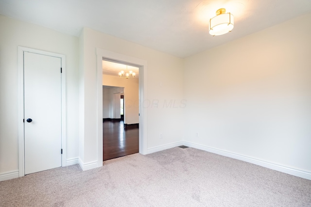 spare room featuring carpet floors, baseboards, and a chandelier