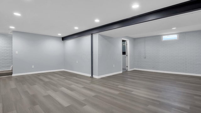basement with recessed lighting, baseboards, dark wood-style floors, and brick wall